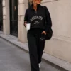 EA-TE536-1 Honoria black slogan co-ord, standing front view of zip-neck top and matching trousers