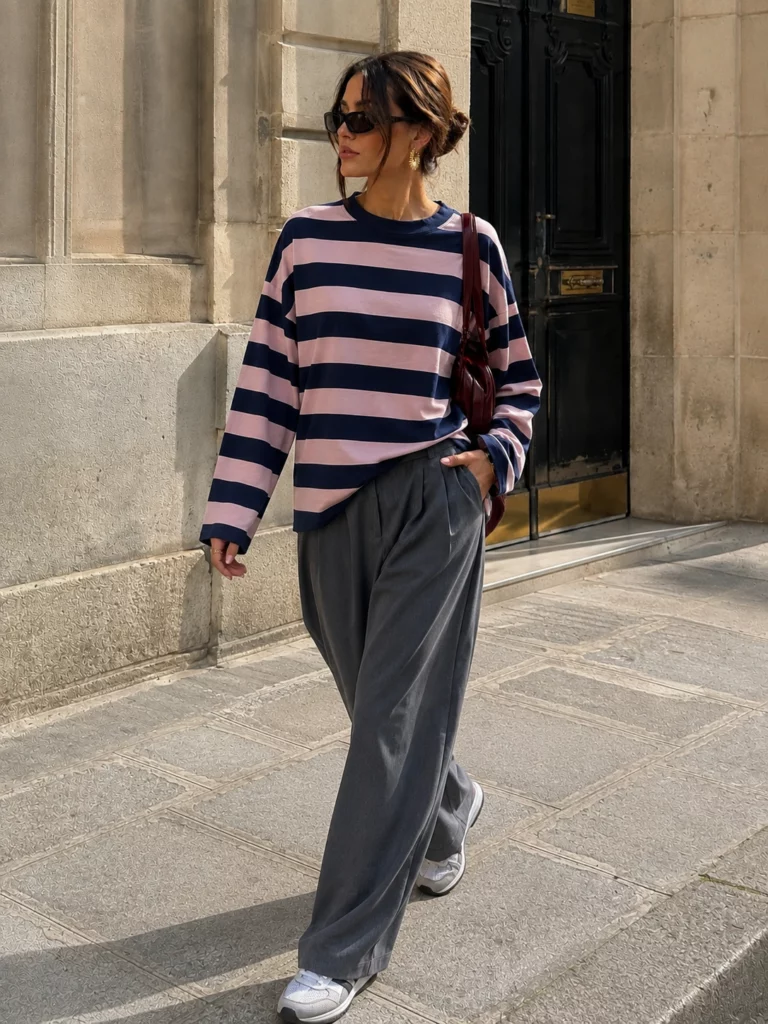 Model wearing the Amelie navy blue and pink striped T-shirt with grey trousers, full-length standing view